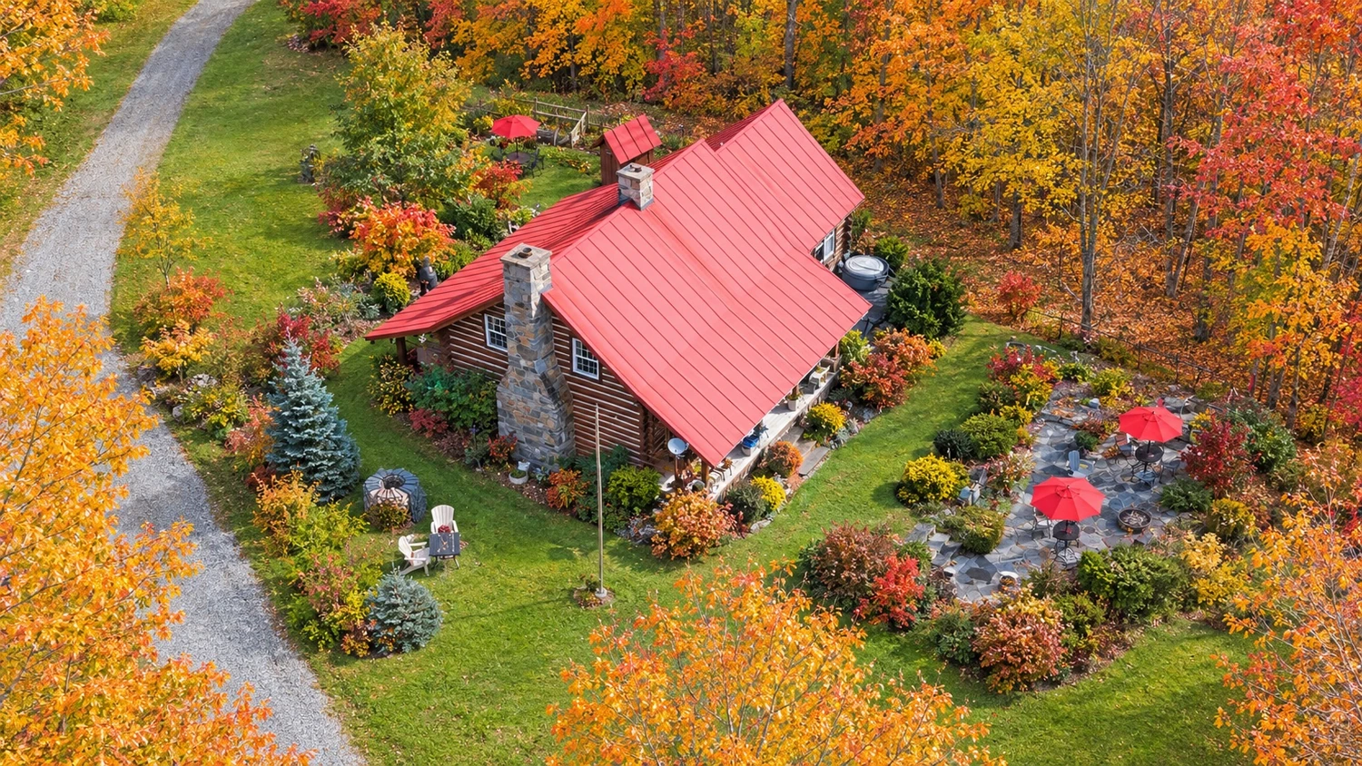 The log home with its red roof, garden terrace and autumn-colored trees, seen from above.